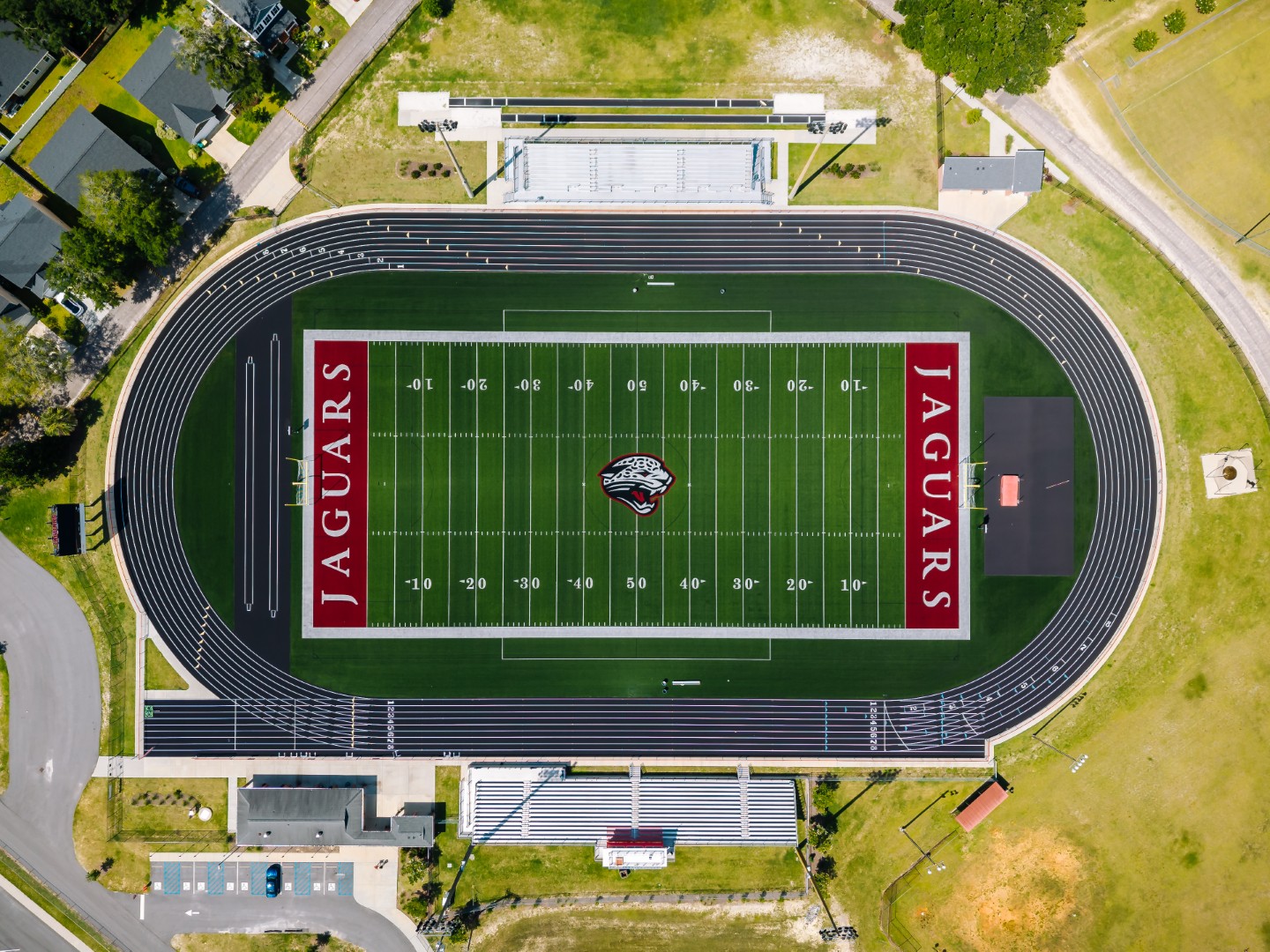 Aerial view of a football stadium with a green field, black running track, red end zones labeled Jaguars, stadium seating on both sides, and surrounding buildings and roads.