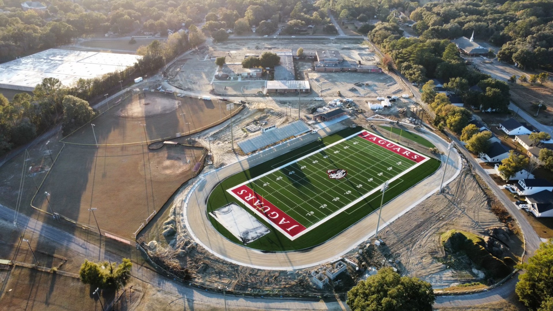 Aerial view of a football stadium with a green turf field labeled Jaguars, surrounded by a running track and construction areas, with trees and buildings in the background.
