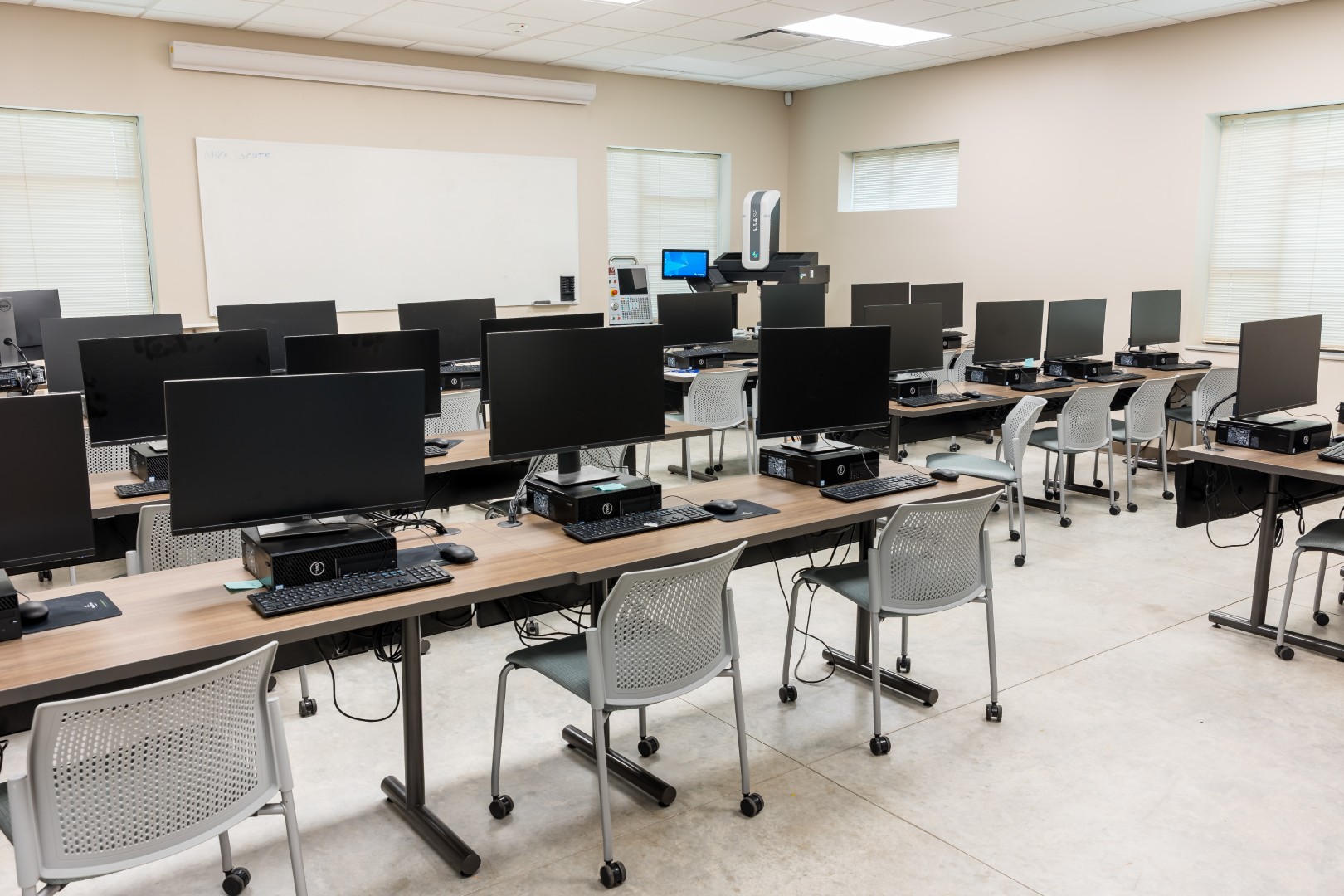 A modern computer lab with rows of desks holding desktop computers and monitors, gray chairs, and a whiteboard.